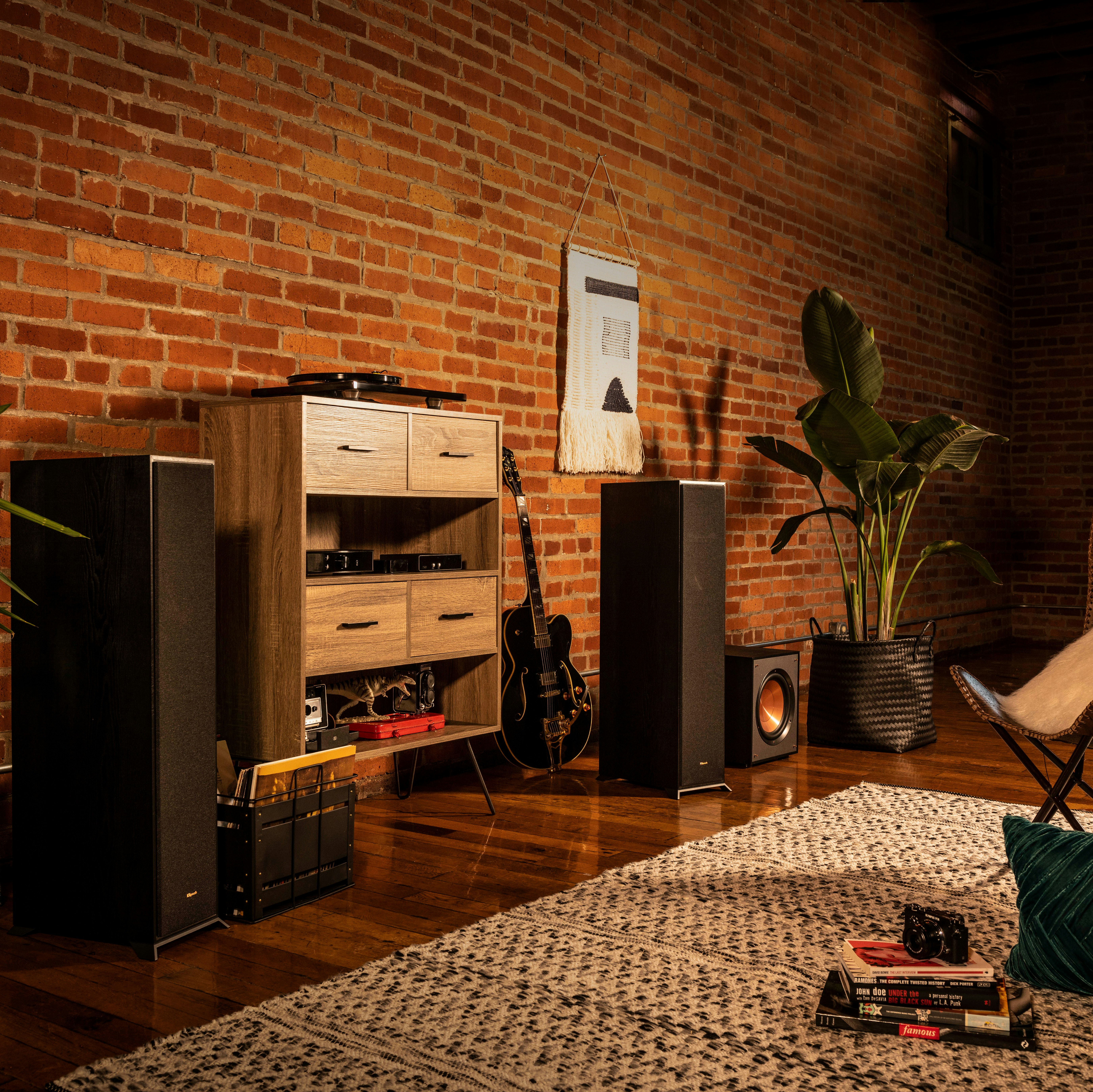 Klipsch Reference floorstanding speakers flanking a wood cabinet a guitar